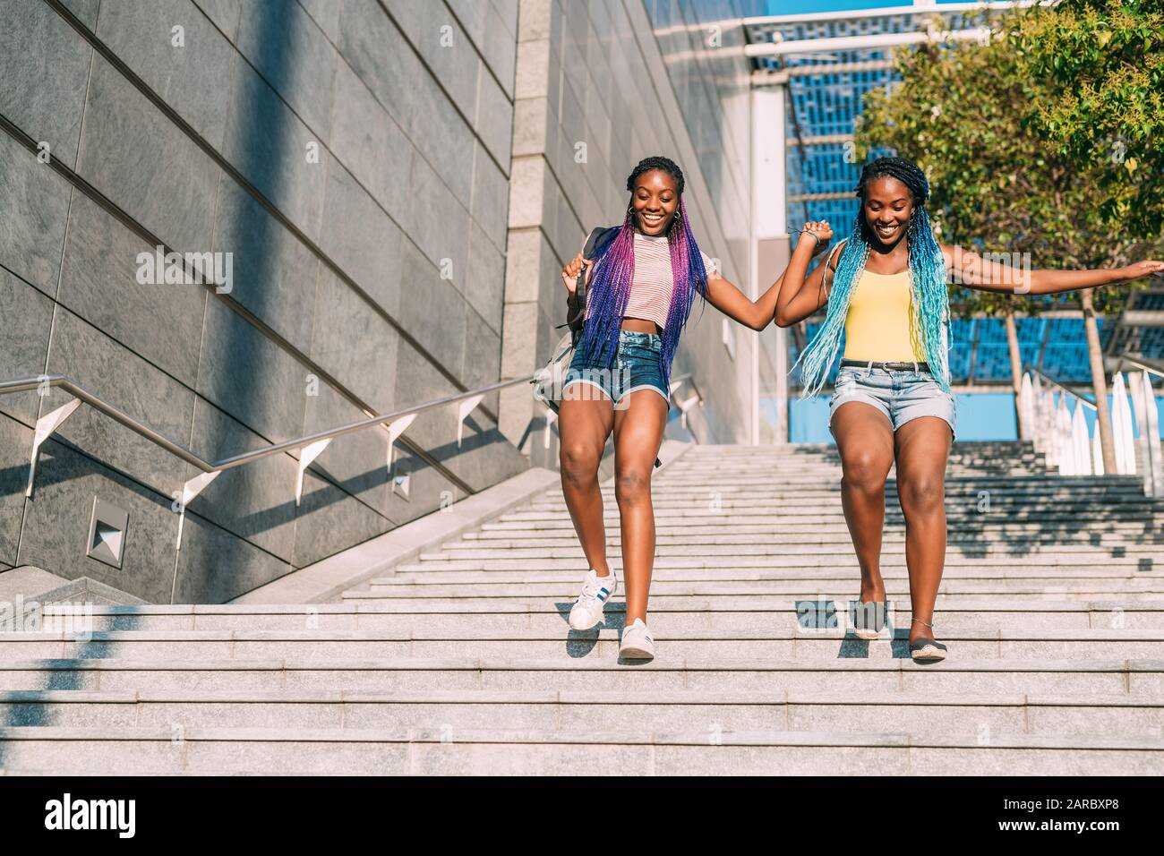 Dos hermosas hermanas negras que caminan abajo juntas sosteniendo las manos - familia, unión, concepto de unión Foto de stock
