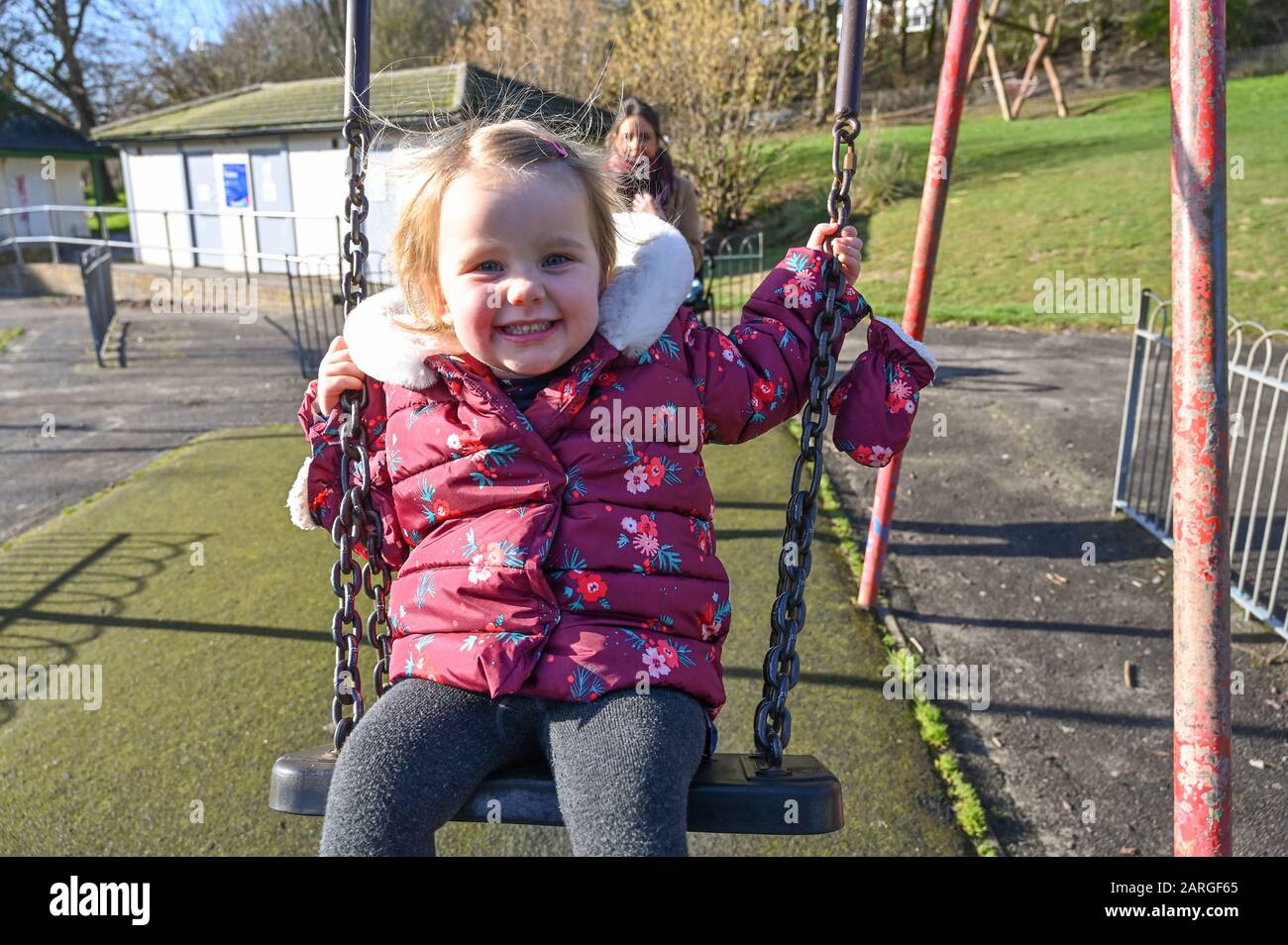 Brighton Reino Unido 28 de enero de 2020 - Isabella de 3 años disfruta de un paseo en los columpios en Queens Park Brighton con su madre empujando en un hermoso día soleado pero frío en Gran Bretaña . Crédito: Simon Dack / Noticias En Vivo De Alamy Foto de stock