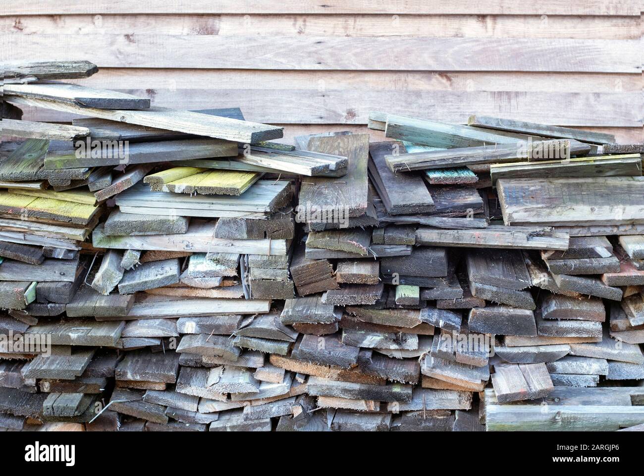 Muchas viejas tablas desgastadas apiladas contra la pared de madera Foto de stock