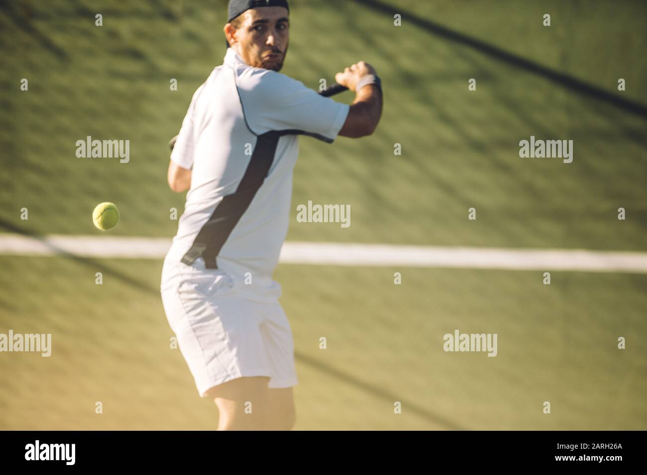 Joven jugador de tenis masculino golpeando una poderosa mano trasera durante un partido. Jugador de tenis jugando al tenis en una pista de tenis. Foto de stock