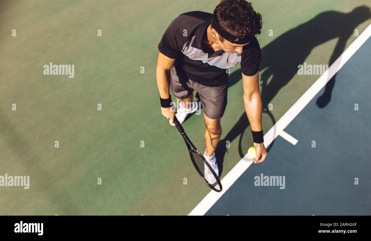 Vista superior de un jugador de tenis joven con raqueta lista para servir una pelota de tenis. Jugador profesional de pie en la línea de base que sostiene la raqueta de tenis y. Foto de stock