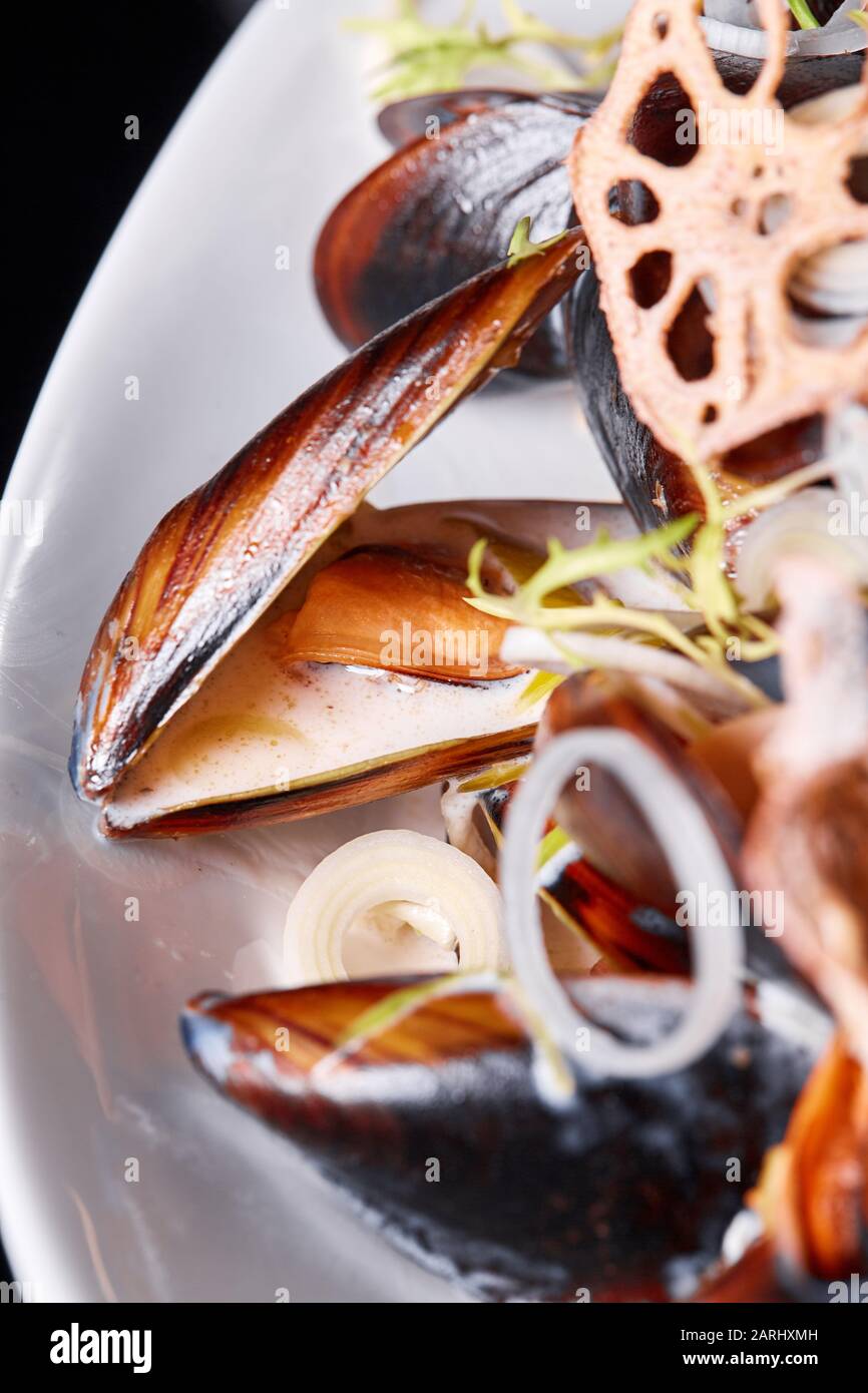 Deliciosos mejillones de marisco con rúcula y cebollas. Limón y baguette . Almejas en las conchas. Menú del restaurante Foto de stock