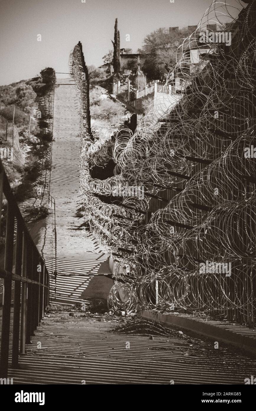 Vista de la cerca fronteriza internacional de EE.UU./México con alambre de navaja siguiendo cuesta arriba con casas mexicanas al otro lado de la cerca de Nogales, AZ, EE.UU., en sí Foto de stock