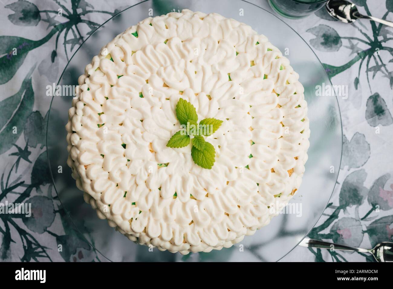 Vista superior de un pastel casero de queso de menta con glaseado blanco y hojas verdes de menta. Servido en un plato de vidrio. Foto de stock