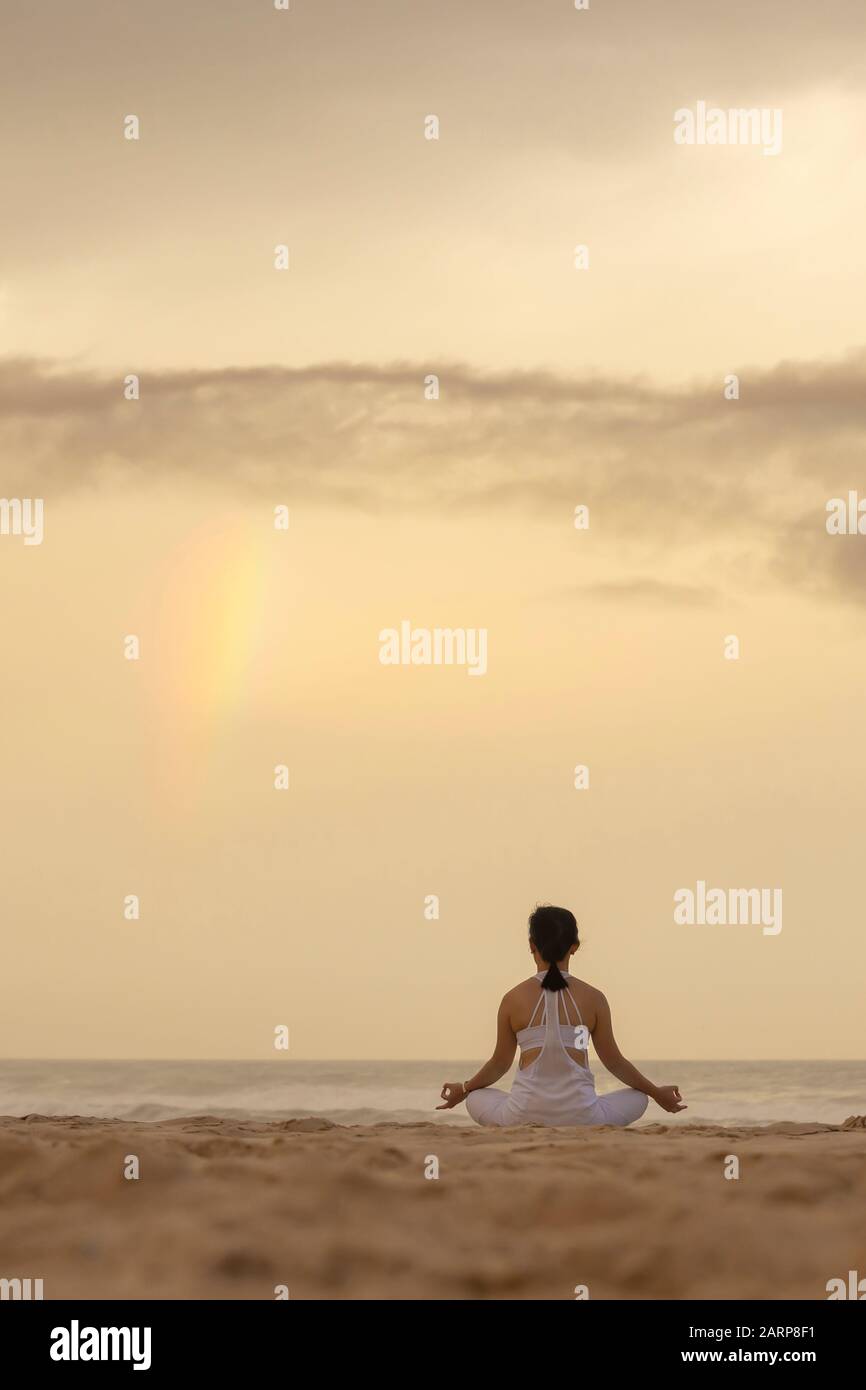 yoga loto pose meditación práctica de la joven mujer en una playa con arco iris Foto de stock