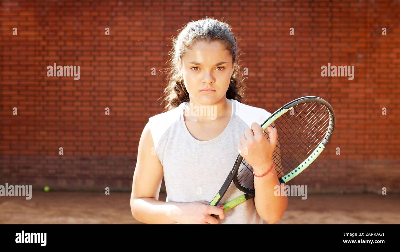 Retrato de la chica de juegos de tenis bastante joven con raqueta en pista de tenis de arcilla naranja Foto de stock