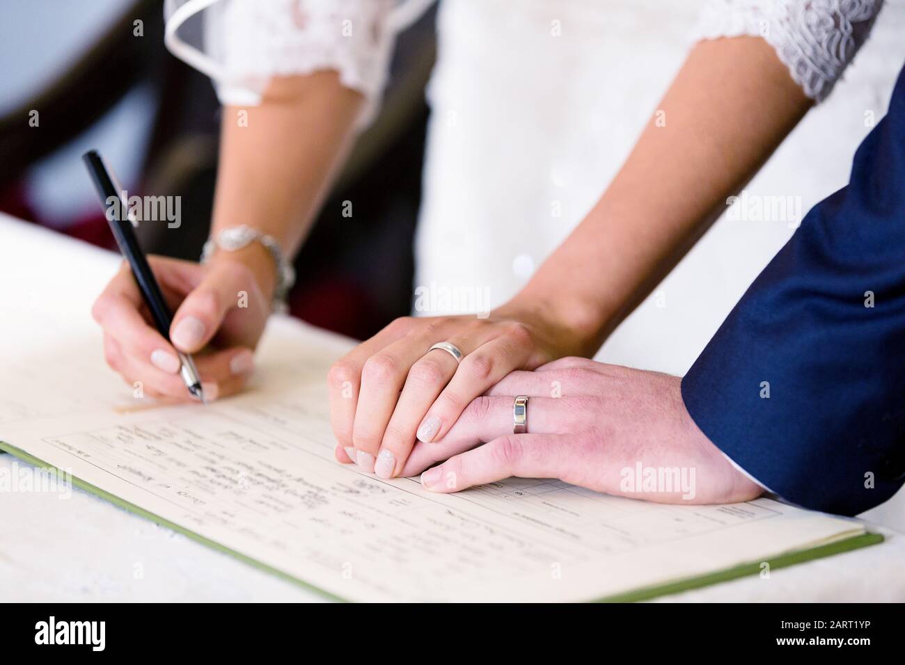 Una novia y un novio firman un libro de registro de matrimonio de la iglesia después de su boda de la iglesia. Ambos anillos de boda son claramente visibles Foto de stock