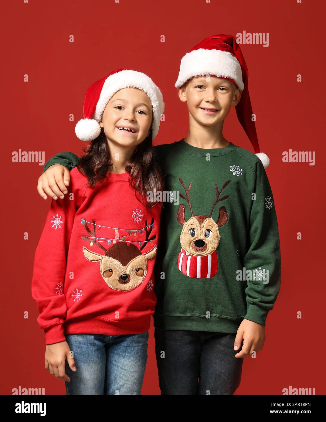 Niños lindos en suéteres de Navidad y gorros de Papá Noel en color de fondo  Fotografía de stock - Alamy