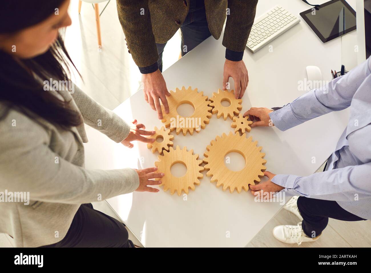 Un grupo de gente de negocios sostiene ruedas de madera con dientes en sus manos en una mesa blanca de oficina. Foto de stock