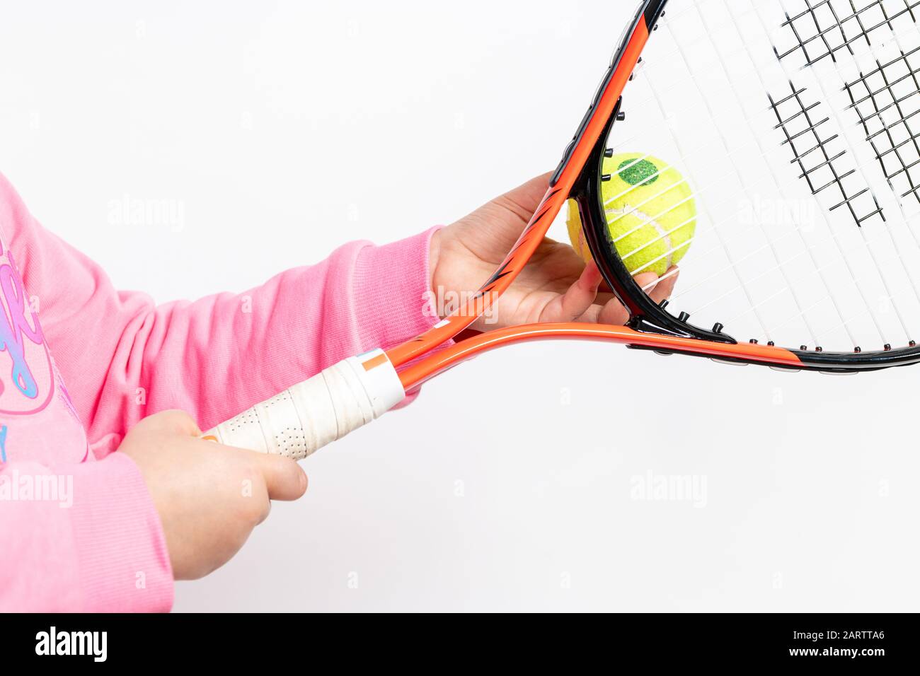 Una chica que lleva una sudadera de color rosa sostiene la raqueta de tenis y la pelota de tenis sobre fondo blanco Foto de stock