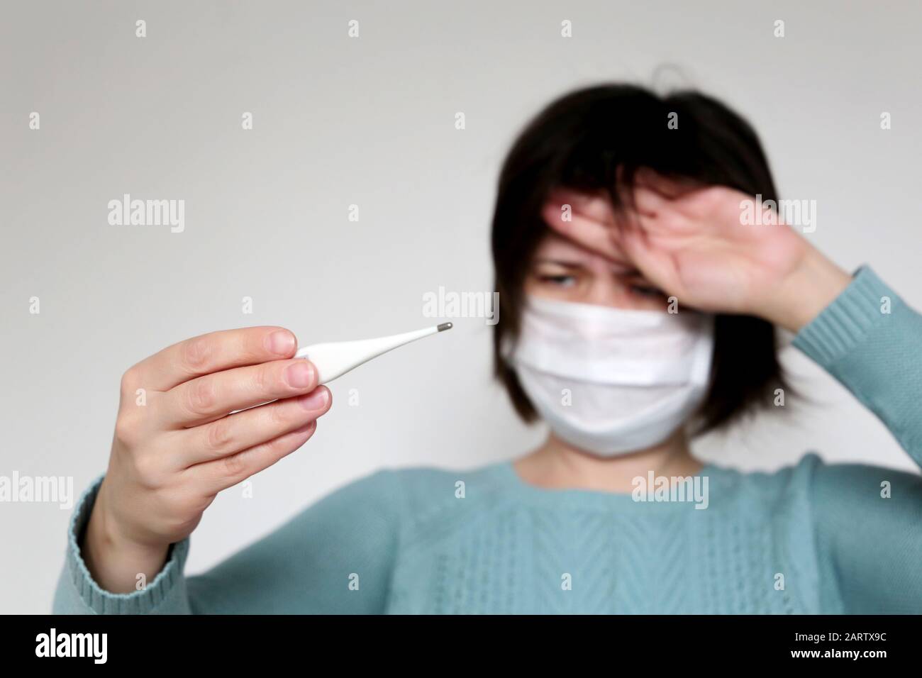 Fiebre y síntomas del coronavirus, la mujer mide la temperatura corporal. Chica preocupada con máscara médica con termómetro Foto de stock