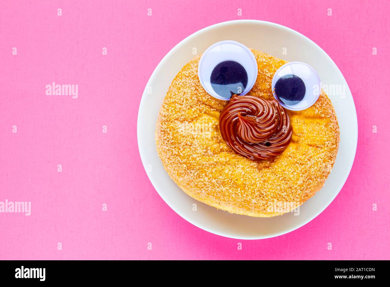 Un Tim Hortons Dulce de leche Donut con bolas de ojo negro de gorgía en un plato con fondo rosa Foto de stock