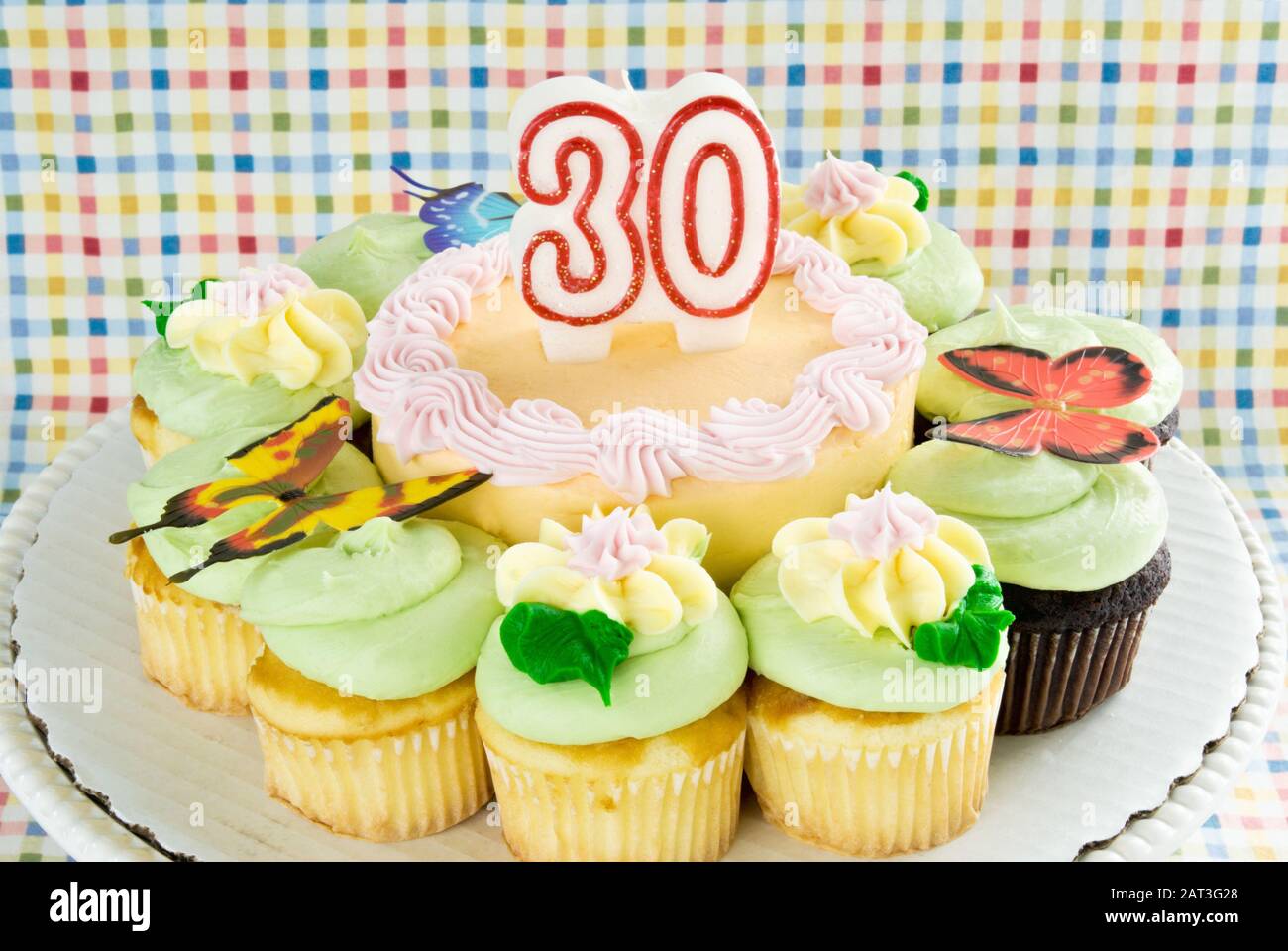 Vista superior de un pastel de cumpleaños y cupcakes en crema de  mantequilla de color pastel en un soporte para pasteles. La vela de cera  número 30 está en la parte superior