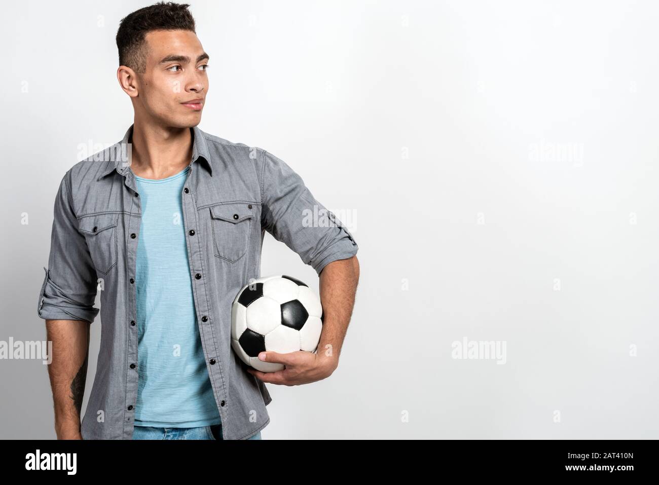 Hombre mulatto vestida con ropa informal de pie sobre fondo blanco de pared  sosteniendo una pelota de fútbol - espacio para copiar Fotografía de stock  - Alamy