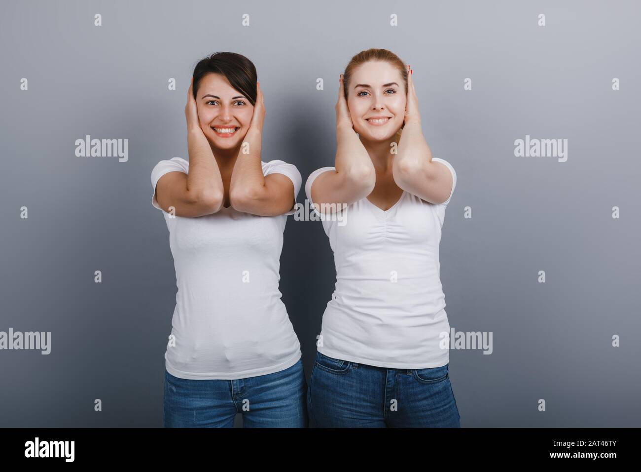 Dos amigos mujeres posando en el estudio cerrando oídos con brazos. Concepto de gestuing - Imagen Foto de stock