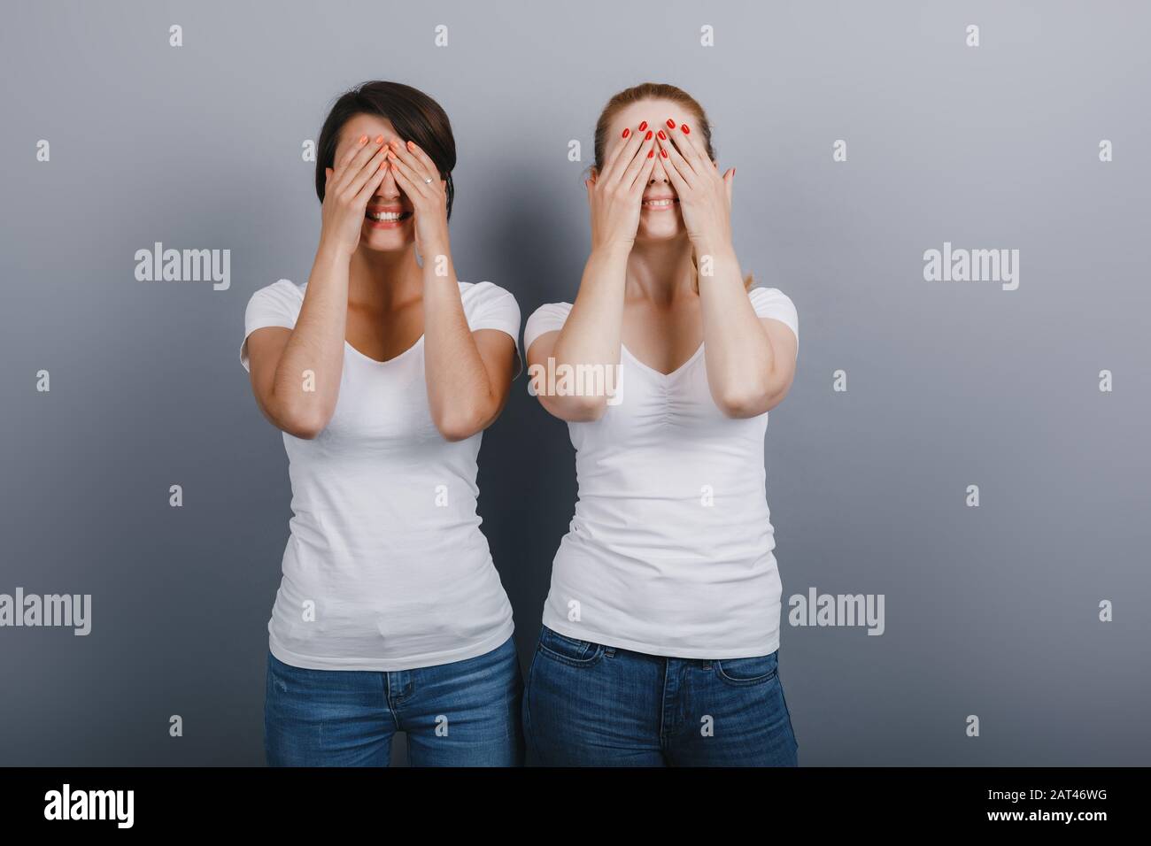 Dos amigos mujeres posando en el estudio cerrando los ojos con los brazos. Concepto de gestuing - Imagen Foto de stock