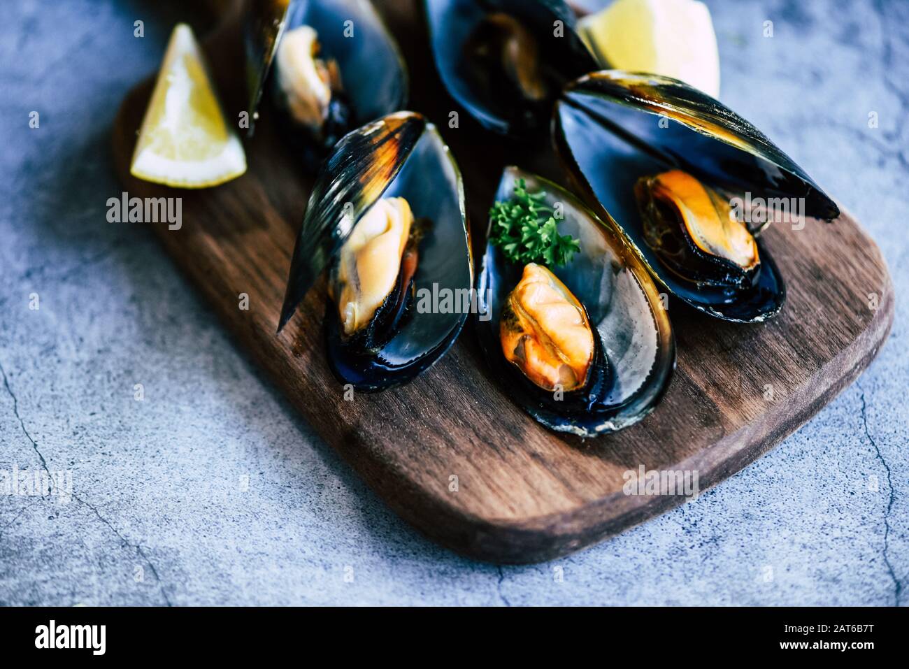 Mejillones cocidos con hierbas de fondo limón y plato oscuro / mariscos frescos en tabla de cortar de madera en el restaurante mejillón de mariscos Foto de stock
