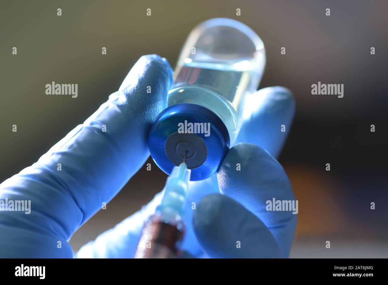 La jeringa extrae el medicamento líquido del vial de color azul en la mano enguantada de la enfermera. Foto de stock