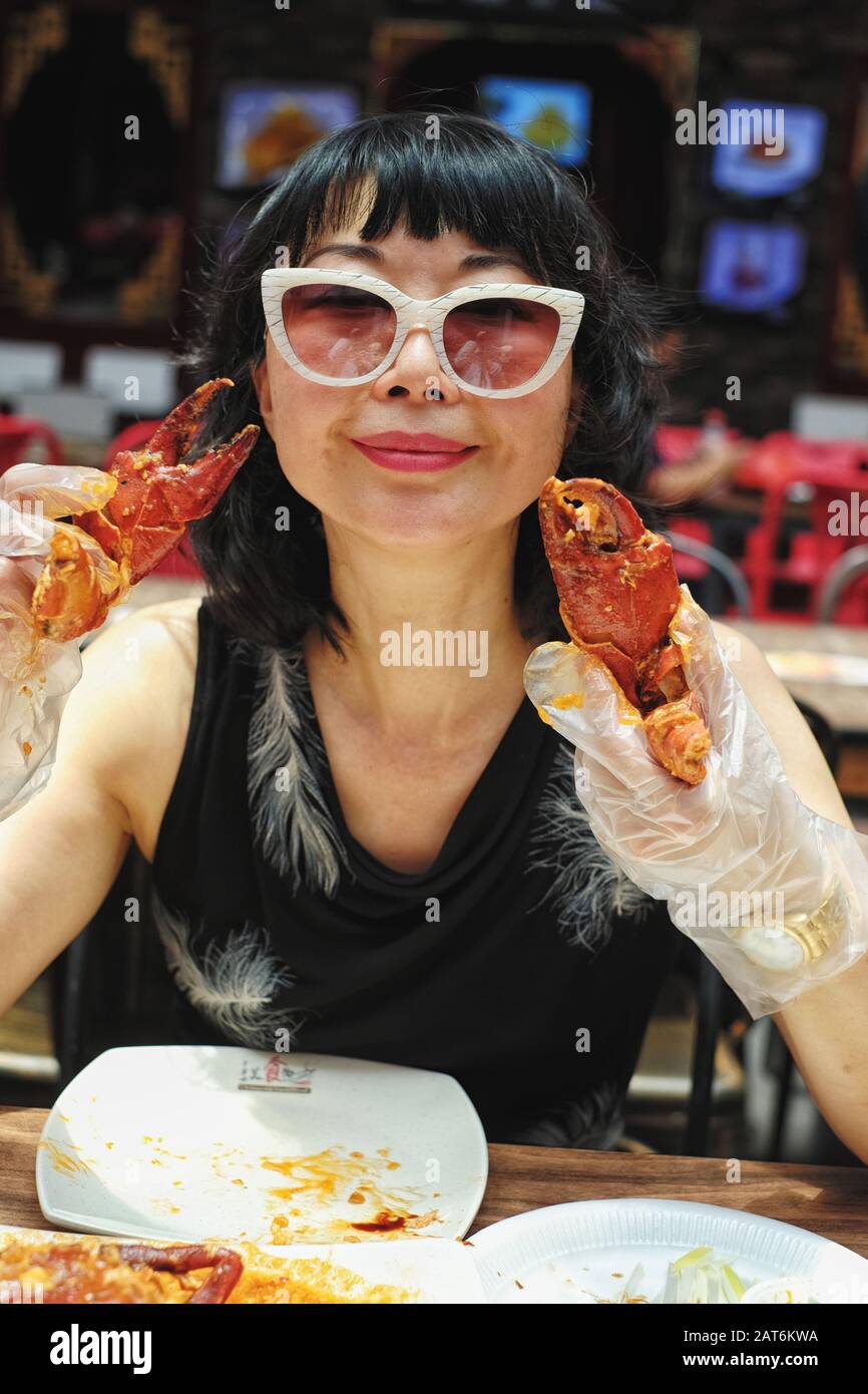 Una mujer china de mediana edad con gafas de sol y guantes de plástico que  come cangrejo de Chile de Singapur en una mesa de comedor con puesto de  comida en la