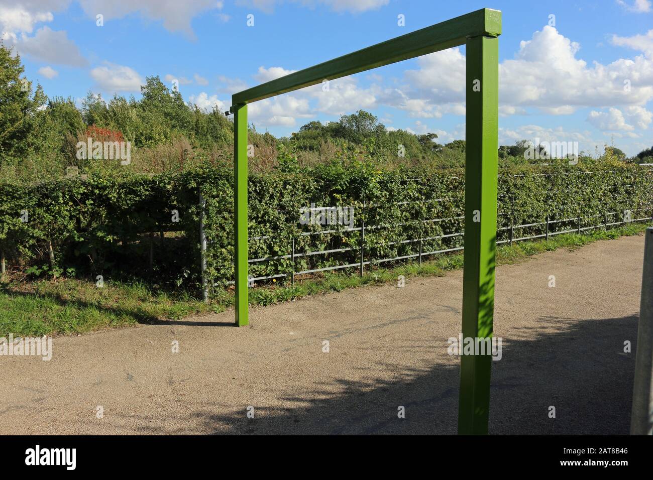 Parque rural verde pintado de metal de la barrera de restricción de altura del aparcamiento, con una valla de metal y cobertura con cielo azul y nube blanca. Foto de stock