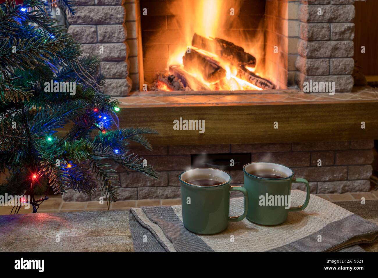 Ambiente acogedor antes de la chimenea y los juguetes decorados con árboles  de Navidad y luces de Navidad con tazas de té en la mesa de madera, en casa  de campo, vacaciones