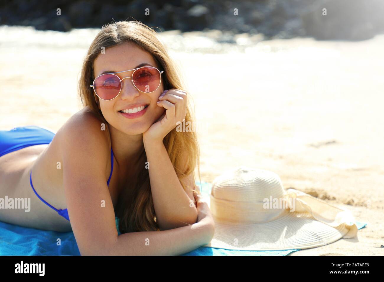 Joven hermosa mujer sonriente disfrutando relajarse tumbado en la playa mirando a la cámara. Concepto de vacaciones de verano. Foto de stock