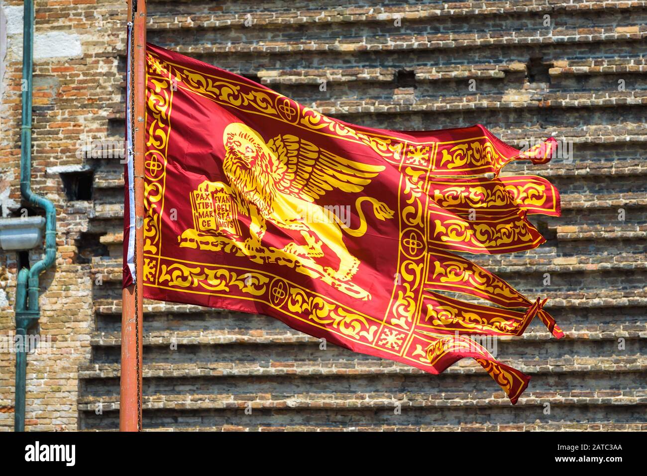 Bandera de Venecia ondeando en la calle en Venecia, Italia. León con alas doradas en la bandera roja, vista de primer plano. La vieja bandera veneciana está en el fondo de la casa vintage wa Foto de stock