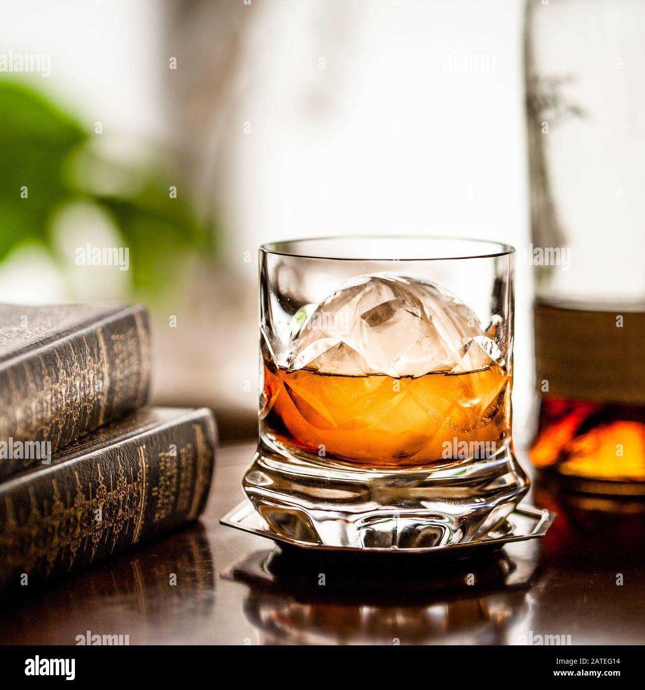 Un cristal de whisky con una gran pieza esférica de hielo y guarnición de cítricos. Foto de stock