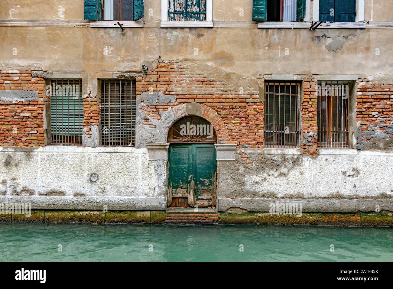 Una antigua puerta verde en un antiguo edificio de almacén da al canal del río de San Marcuola, el distrito de Cannaregio, Venecia, Italia Foto de stock