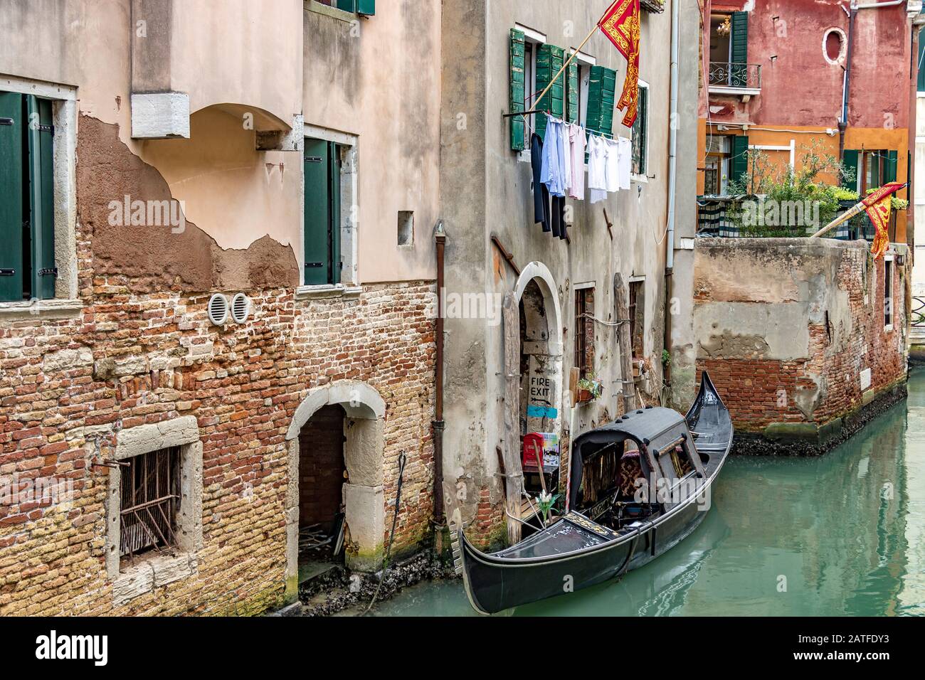 Góndola con un techo amarrado por una casa con persianas verdes y lavado colgando en una línea para secar y la bandera veneciana volando fuera, Venecia, Italia Foto de stock