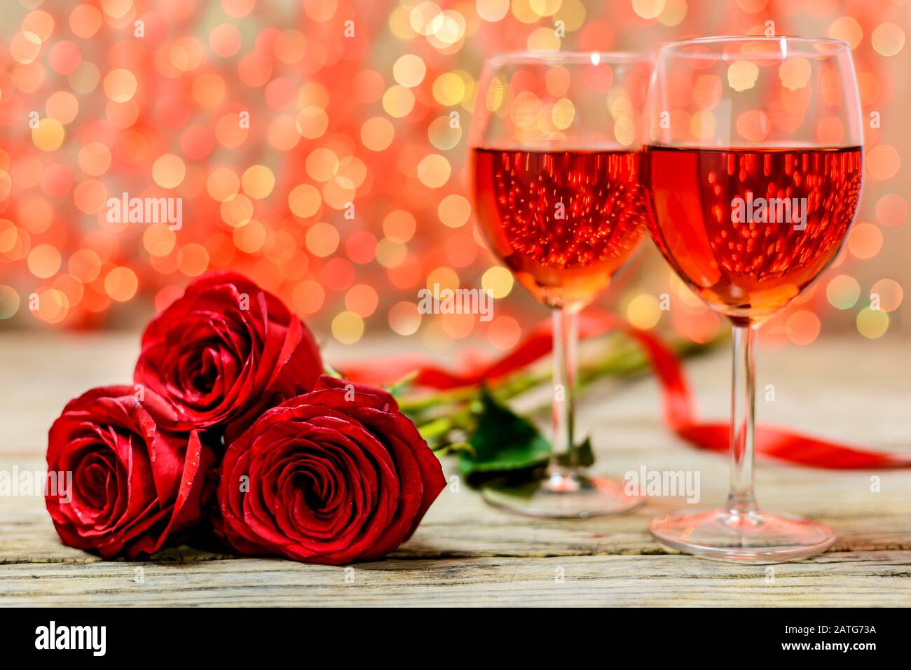 Concepto del día de San Valentín. Dos copas de vino y rosas rojas en una antigua mesa de madera frente a un fondo luminoso difuminado con espacio para texto. S Foto de stock