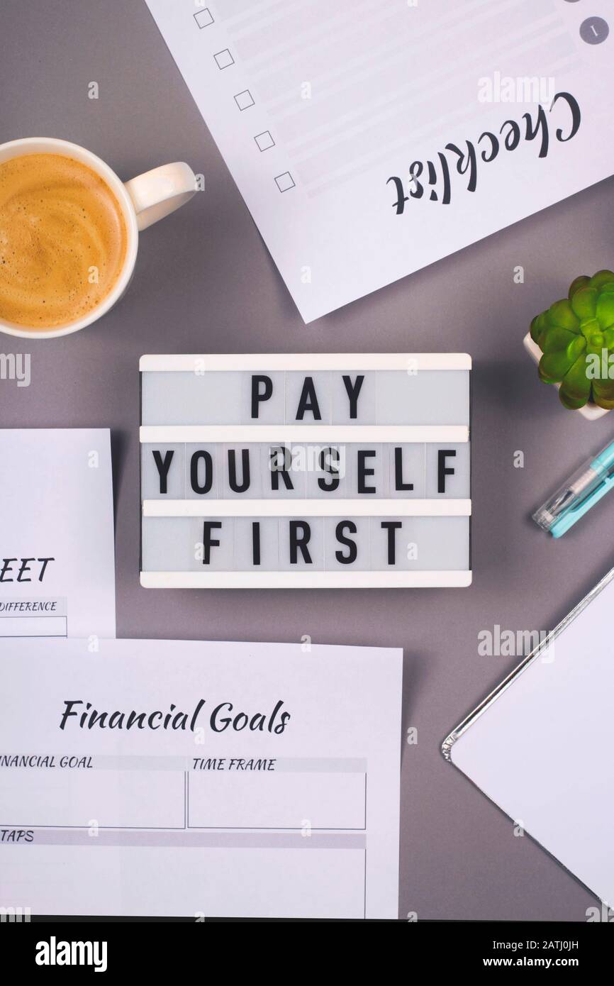 Pague primero. Está escrito en un panel decorativo en el lugar de trabajo gris de un freelancer que cuenta las finanzas y hace ahorros. Foto de stock