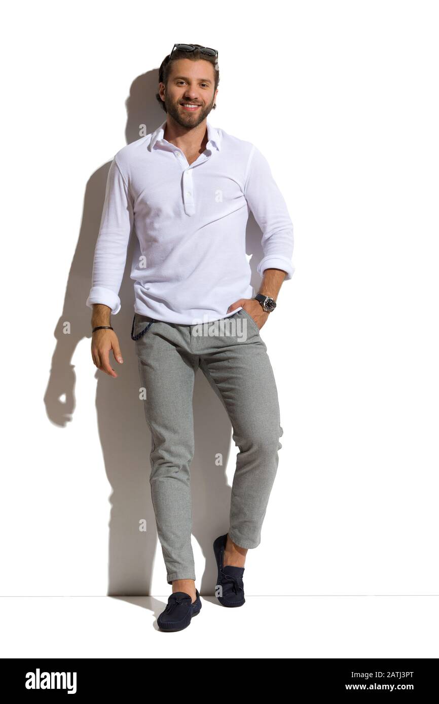 Uluru gobierno Puntuación Un hombre guapo con camisa blanca, pantalones grises y mocasines se inclina  contra la pared soleada y sostiene la mano en el bolsillo. Vista frontal.  Estudio completo Fotografía de stock - Alamy