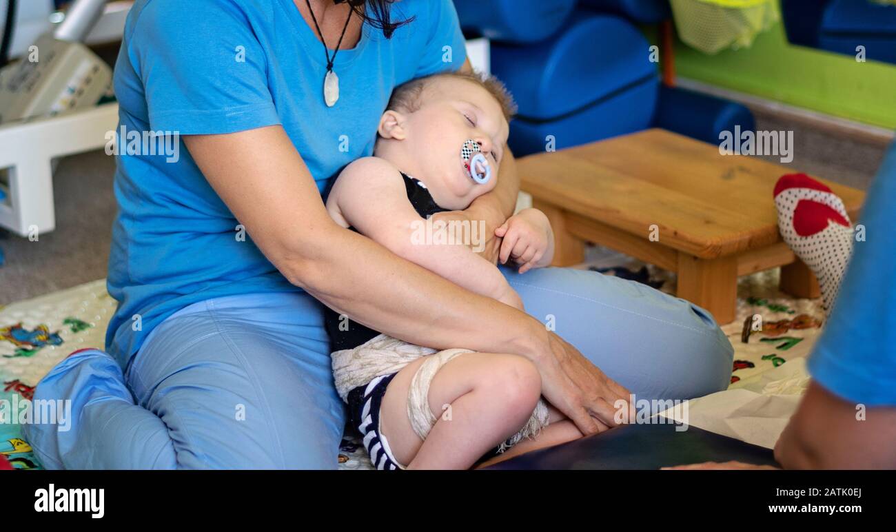 Retrato de un bebé cansado con parálisis cerebral en fisioterapia en un centro de rehabilitación. El niño con discapacidad tiene terapia haciendo ejercicios. Agotar Foto de stock