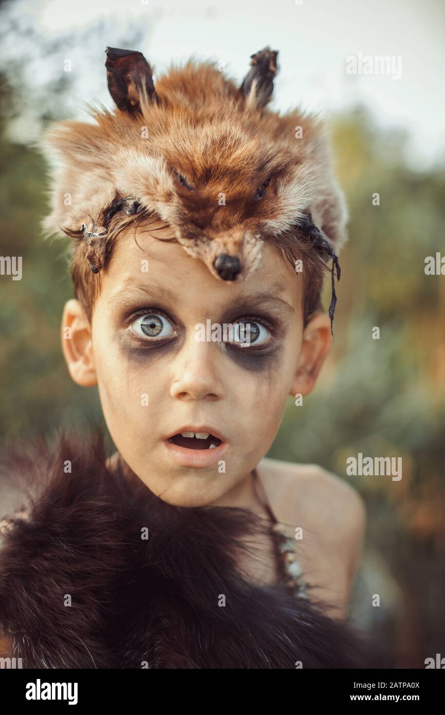 Sorprendió divertido retrato de niño. Pequeño caveman con boca abierta.  Niño tribal prehistórico al aire libre en la naturaleza. Jovencitos y  salvaje sucio, rostro guerrero y cazador. Hombre primitivo de la edad