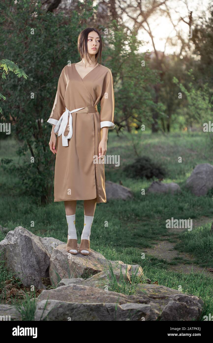 Mujer asiática con kimono japonés tradicional de moda al aire libre en el parque. Elegante y elegante modelo japonés posando al aire libre con un vestido moderno. Joven sonriente niña de pie Mujer asiática con kimono japonés tradicional de moda al aire libre en el parque. Elegante y elegante modelo japonés posando al aire libre con un vestido moderno. Joven sonriente niña de pie