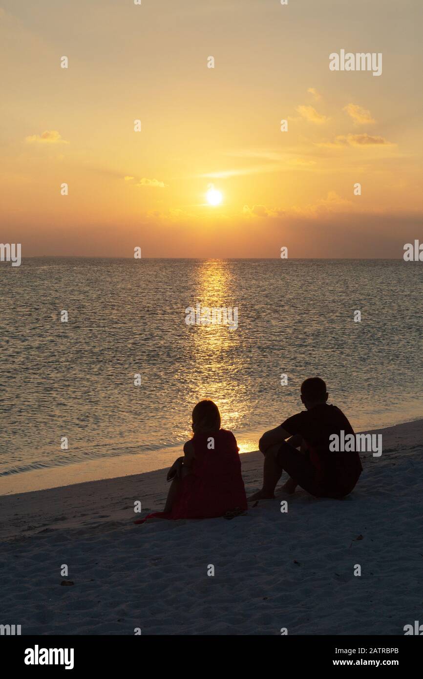 Vacaciones románticas - una pareja sentada en una playa mirando la puesta de sol sobre el Océano Índico, las Maldivas, Asia Foto de stock