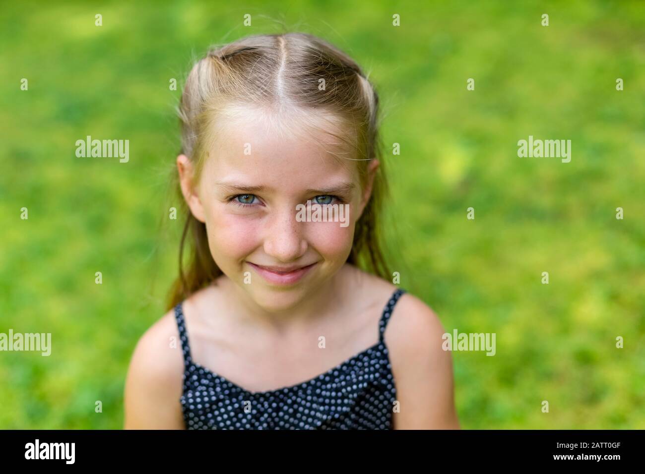 Retrato de una joven con pelo rubio y ojos azules mirando a la cámara con hierba verde brillante como fondo; Columbia Británica, Canadá Foto de stock