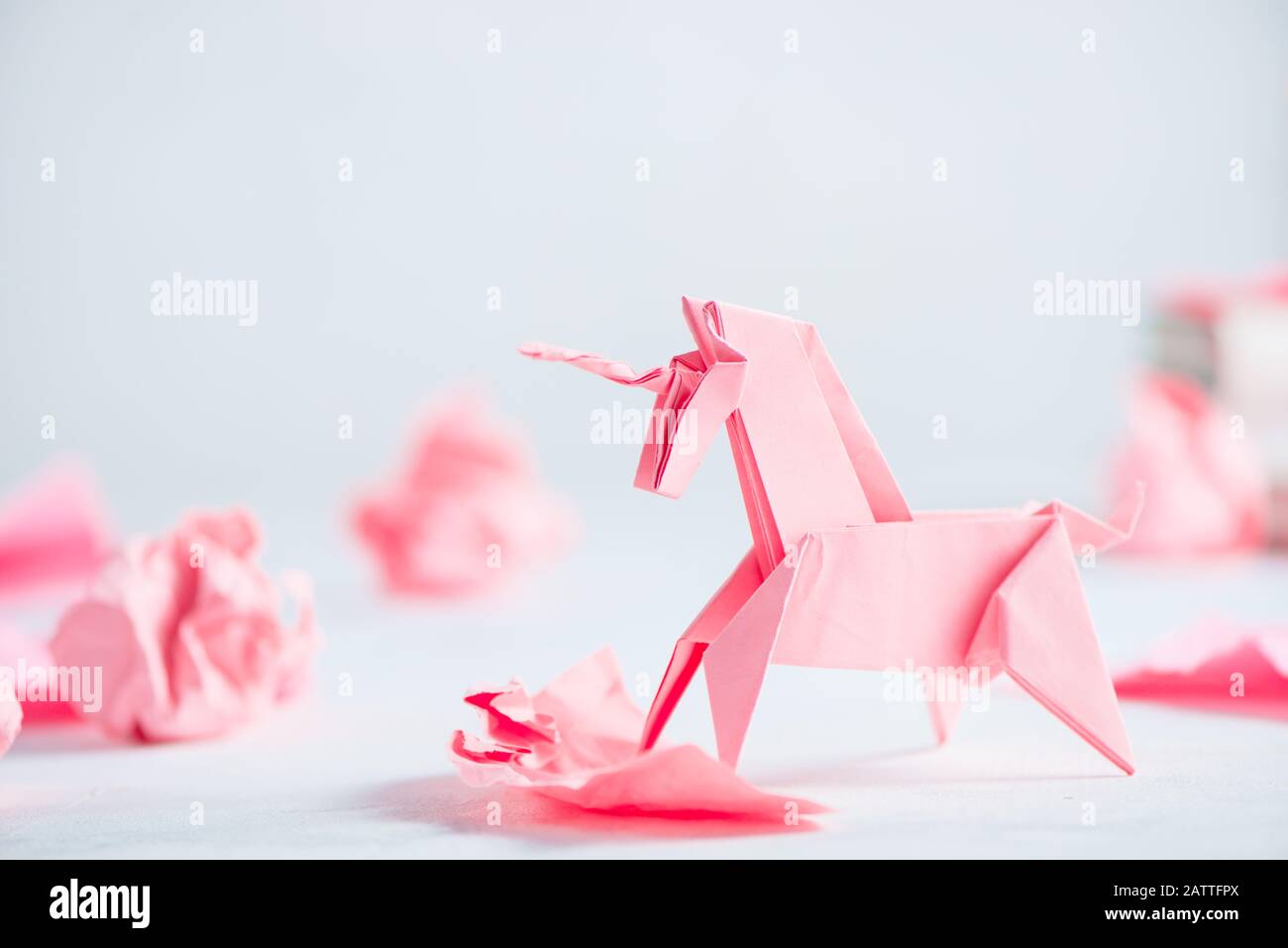 Unicornio de origami rosa con bolas de papel arrugadas. El proceso creativo es la escritura, el fondo ligero Foto de stock