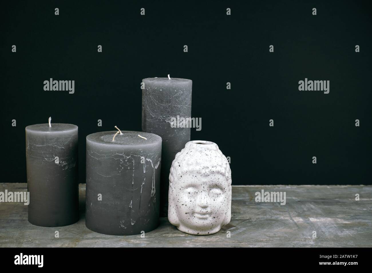 Velas grises y cabeza blanca de Buda de cerámica en una mesa frente a la pared negra Foto de stock