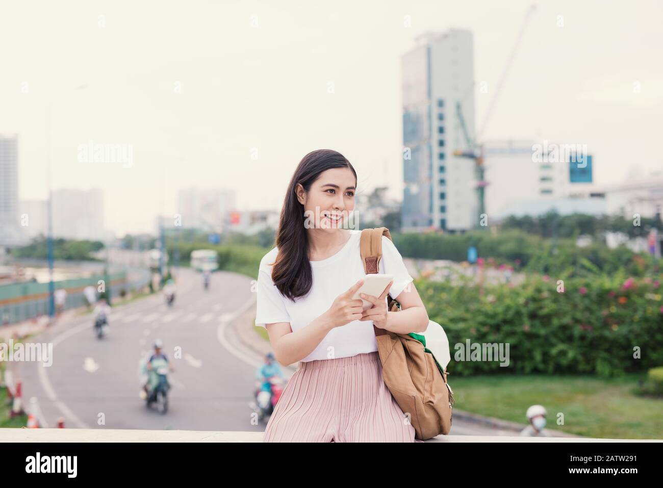 Mujer joven con un teléfono inteligente sentarse con bolsa en ciudad antecedentes Foto de stock