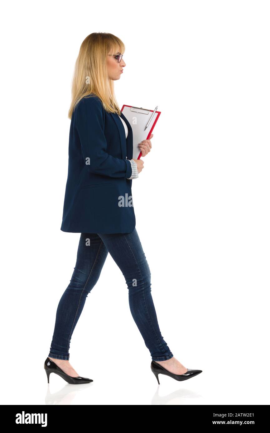 La joven mujer de negocios mugrienta en traje azul y tacones altos está caminando con el portapapeles. Estudio de fondo blanco aislado. Foto de stock