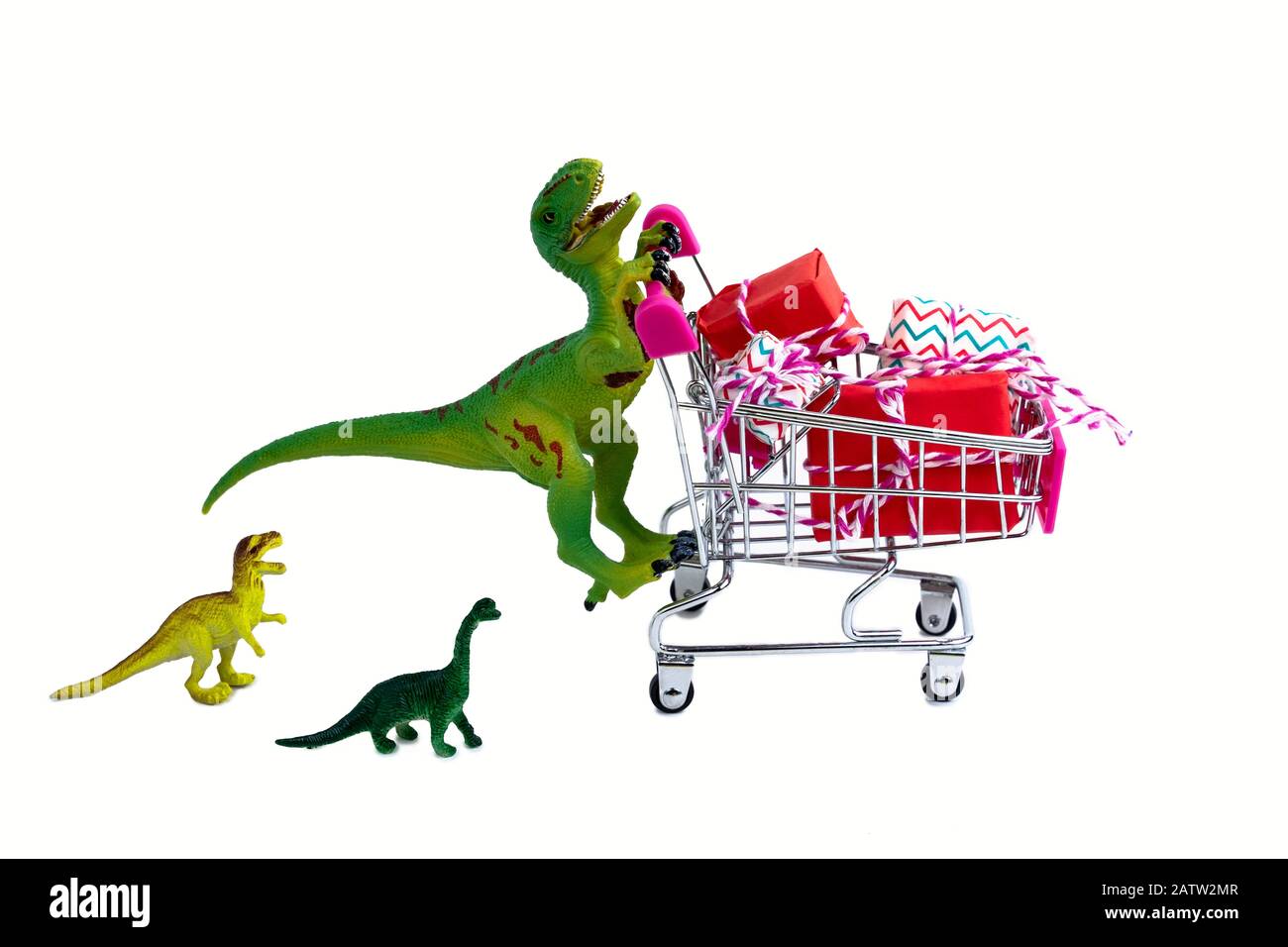 divertido dinosaurio verde juguete con carrito de compras lleno de cajas presentes y pequeños dinosaurios niños aislados sobre fondo blanco Foto de stock