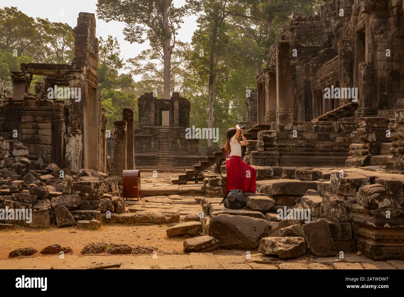 Joven turista en vestido rojo tomando una foto del histórico templo Bayon de piedra, con su cámara dslr, Angkor Wat, Siem Reap, Camboya. Foto de stock