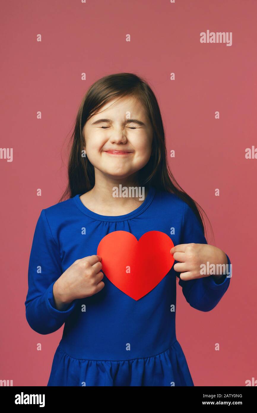 Graciosa niña encantada con San Valentín recibido. Vestido azul y corazón rojo. Concepto del día de San Valentín, amor por todas las edades. Foto de stock