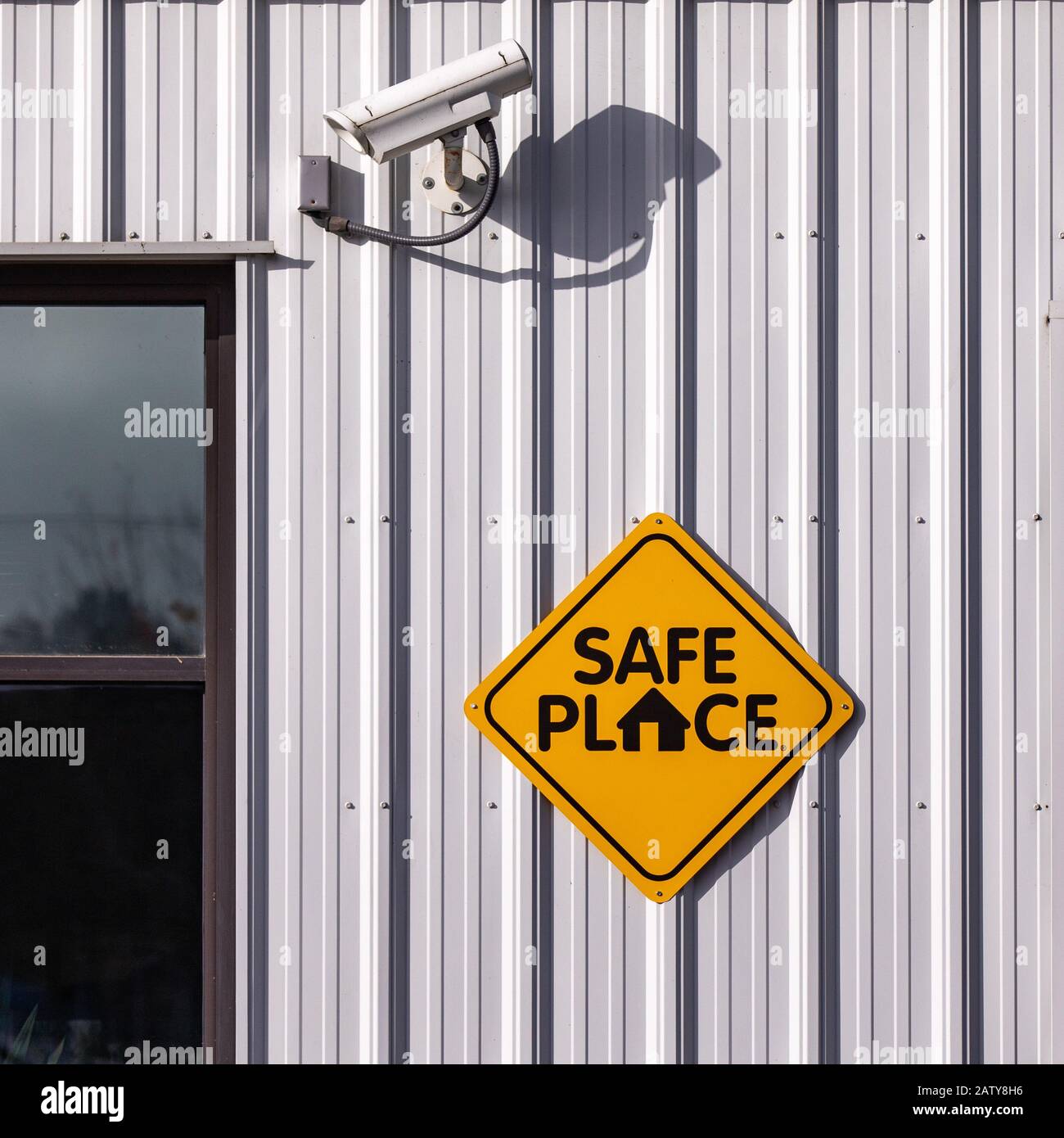 Señal de lugar seguro de una pared de metal claro de un edificio con una cámara de seguridad CCTV encima de él. Foto de stock