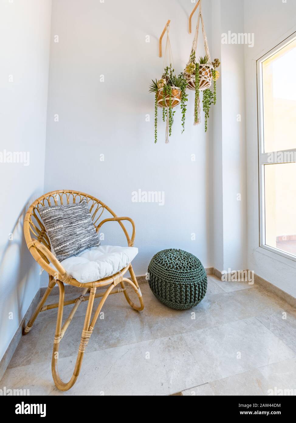 Interior de la con silla ratán con cojín, plantas colgantes macrame y bolsa de fibra en una sala de estar con una gran ventana. Sala de conferencias. Boho sty Fotografía