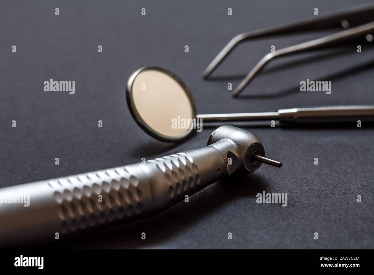 Conjunto de instrumentos dentales metálicos para el tratamiento dental. Pieza dental de alta velocidad, espejo dental y pinzas sobre fondo negro. Herramientas médicas. Shal Foto de stock