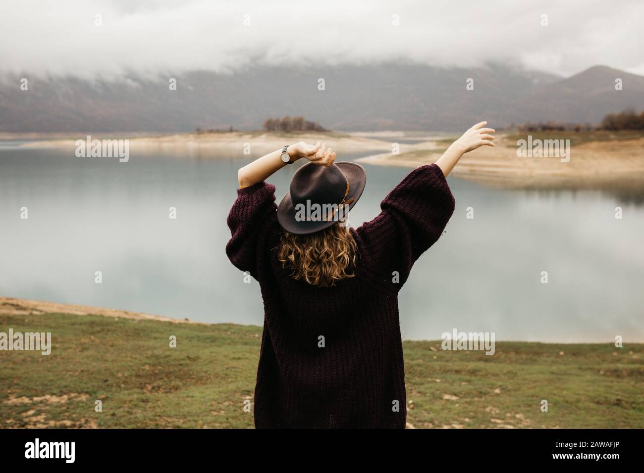 Mujer turística explorando el lago. Ella está de pie girada hacia atrás y mirando a distancia, con sus manos en el aire. Foto de stock