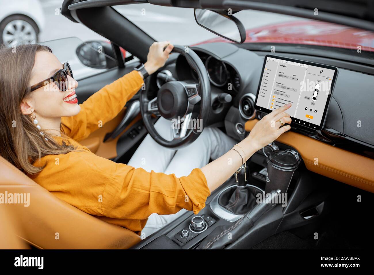 Alegre mujer que controla el coche con un tablero digital, cambiando el modo de piloto automático mientras conduce un cabriolet. Concepto de coche inteligente Foto de stock